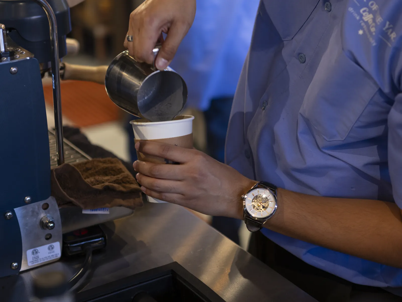 Barista pouring steamed milk into a Back of the Yards cup